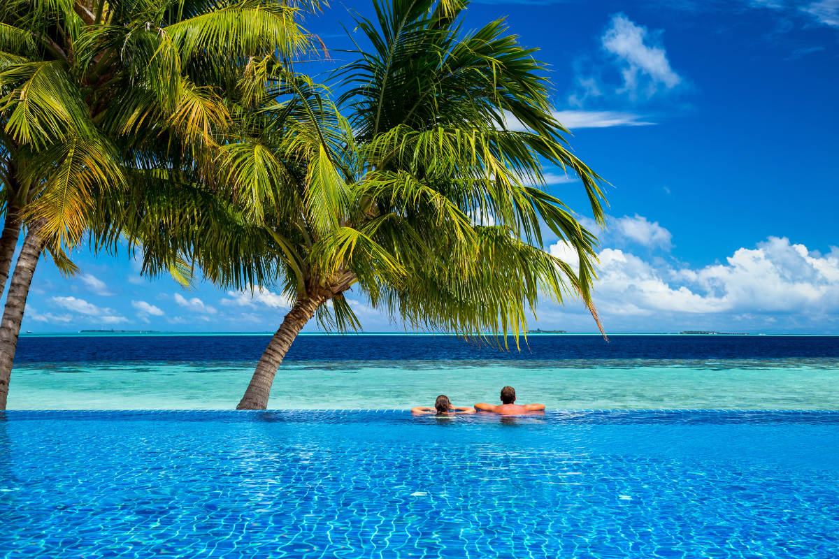 Couple relaxing in an infinity pool overlooking a tropical ocean with palm trees